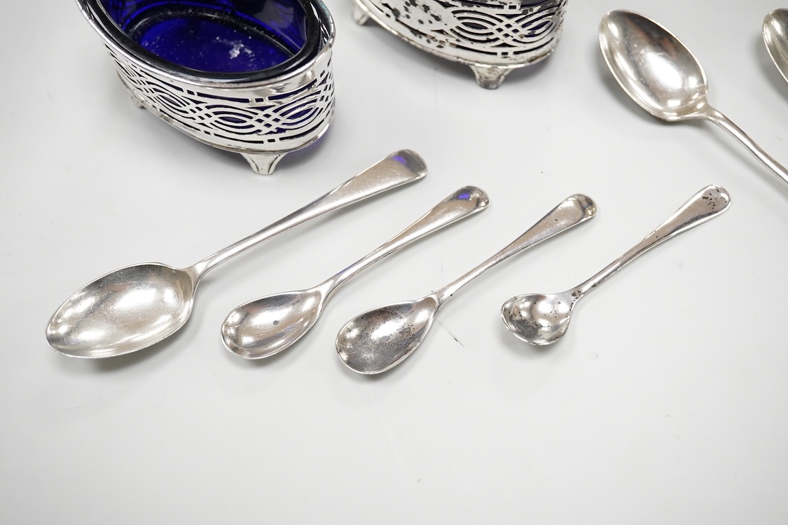 An ornate Edwardian silver oval mustard pot and matching spoon by Barker Brothers, Birmingham, 1902, length, 95mm, together with five other assorted silver condiments including a pair of pierced oval salts with blue glas